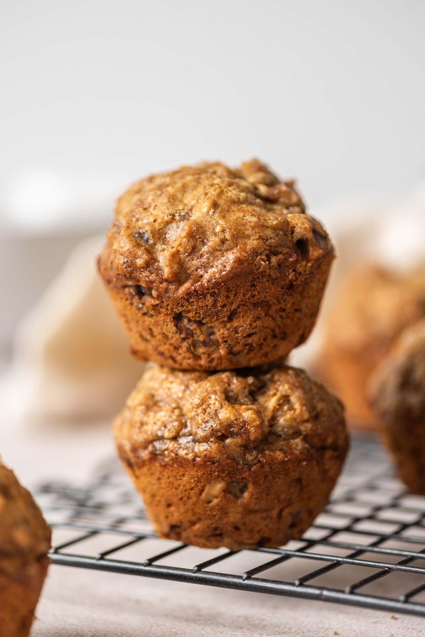 Eierlose Piesangmuffins 2 Twee piesang-okkerneutmuffins bo-op mekaar gestapel op 'n draadrak.