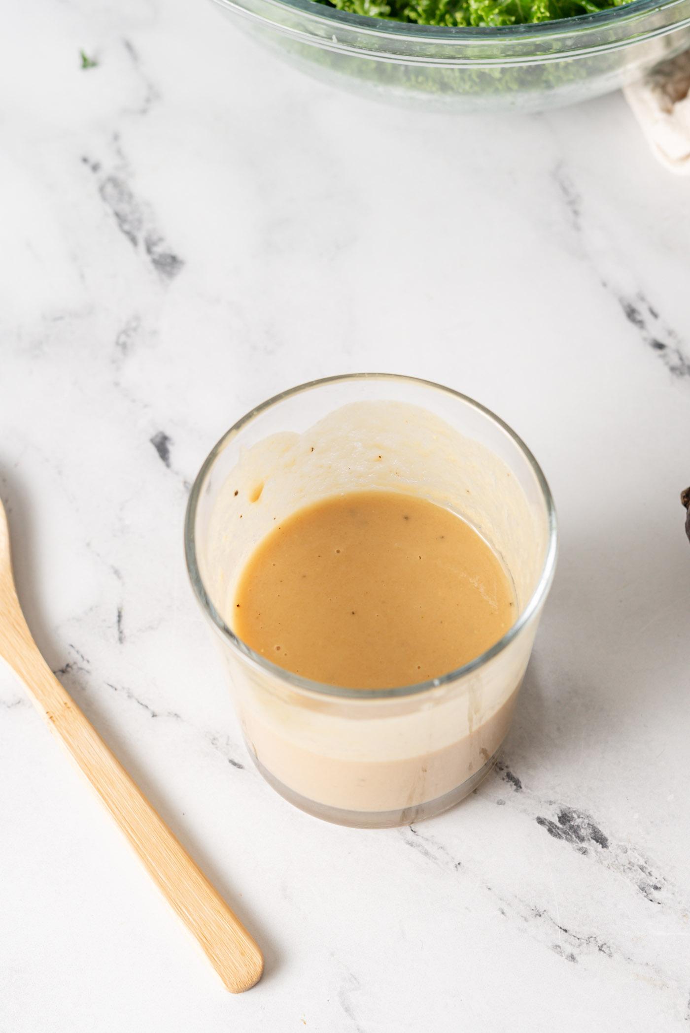 Oorhoofse aansig van 'n fles romerige esdoorn-tahini-dijon-slaaisous met 'n klein houtlepel langs dit.