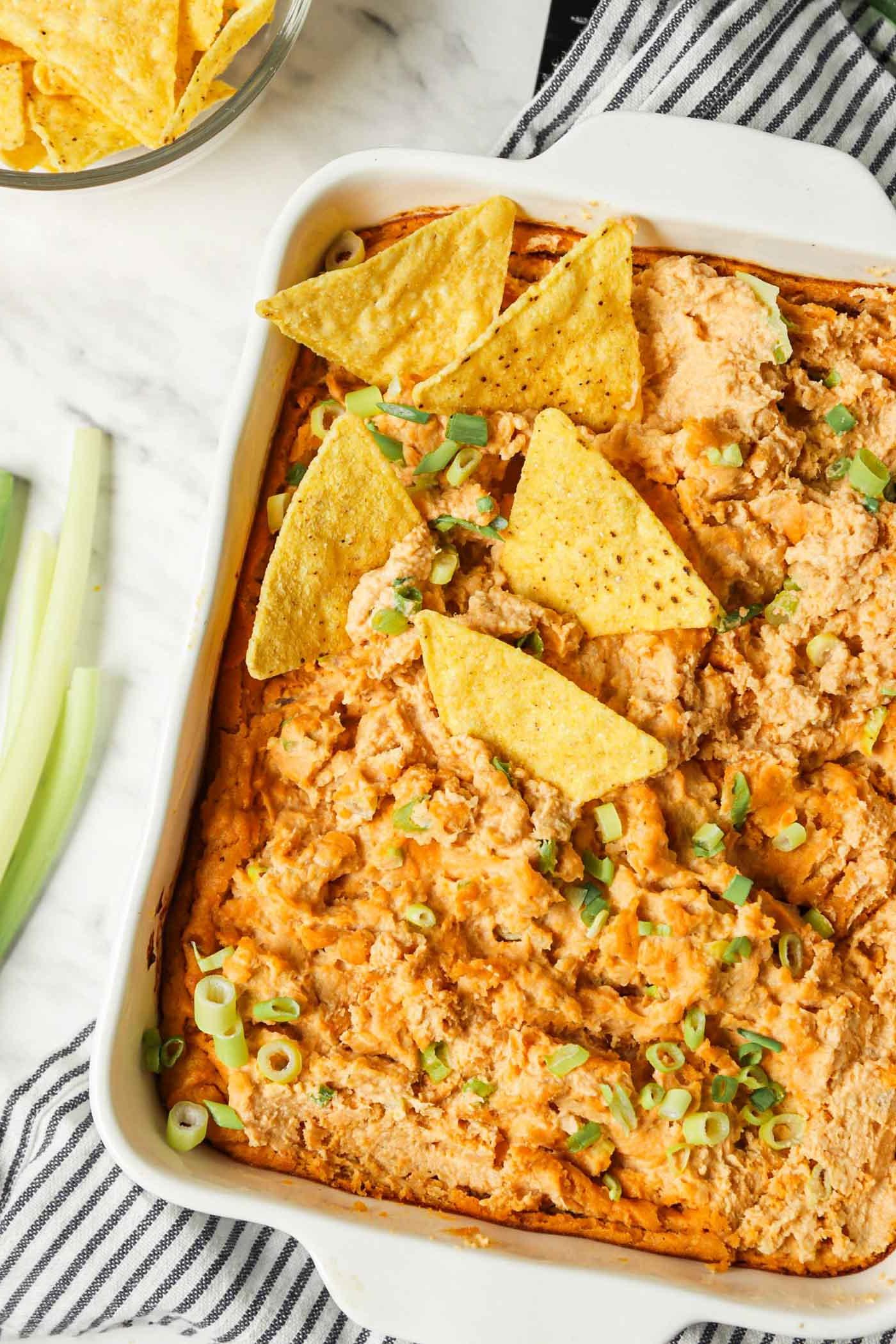 Vegan Buffels Dip 2 Oorsig van 'n bak gebakte buffel dip bedek met sprietui met 'n paar tortillaskyfies in die dip.