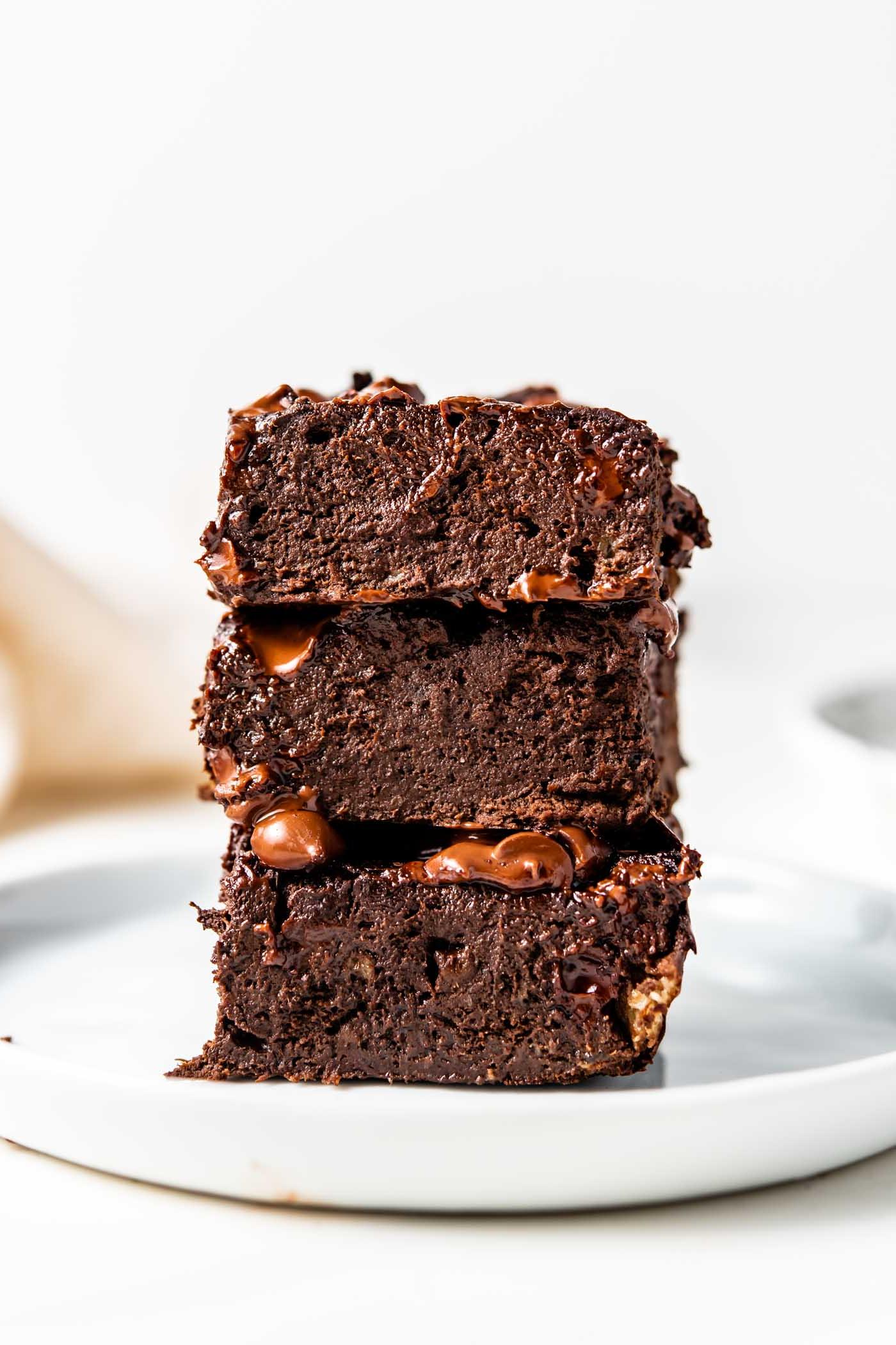 Stack of 3 chocolate brownies on a small white plate.