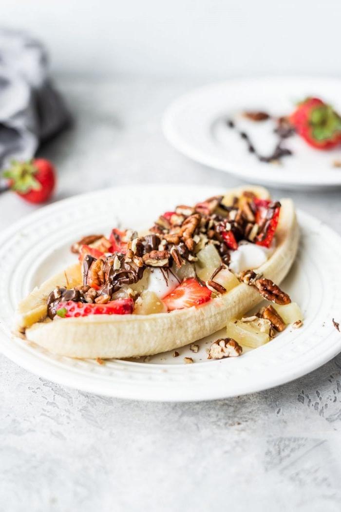 Gesonde Veganistiese Piesangsplit 2 ’n Vegan piesangsplit met suiwelvrye jogurt, pekannote en aarbeie op ‘n wit bord.