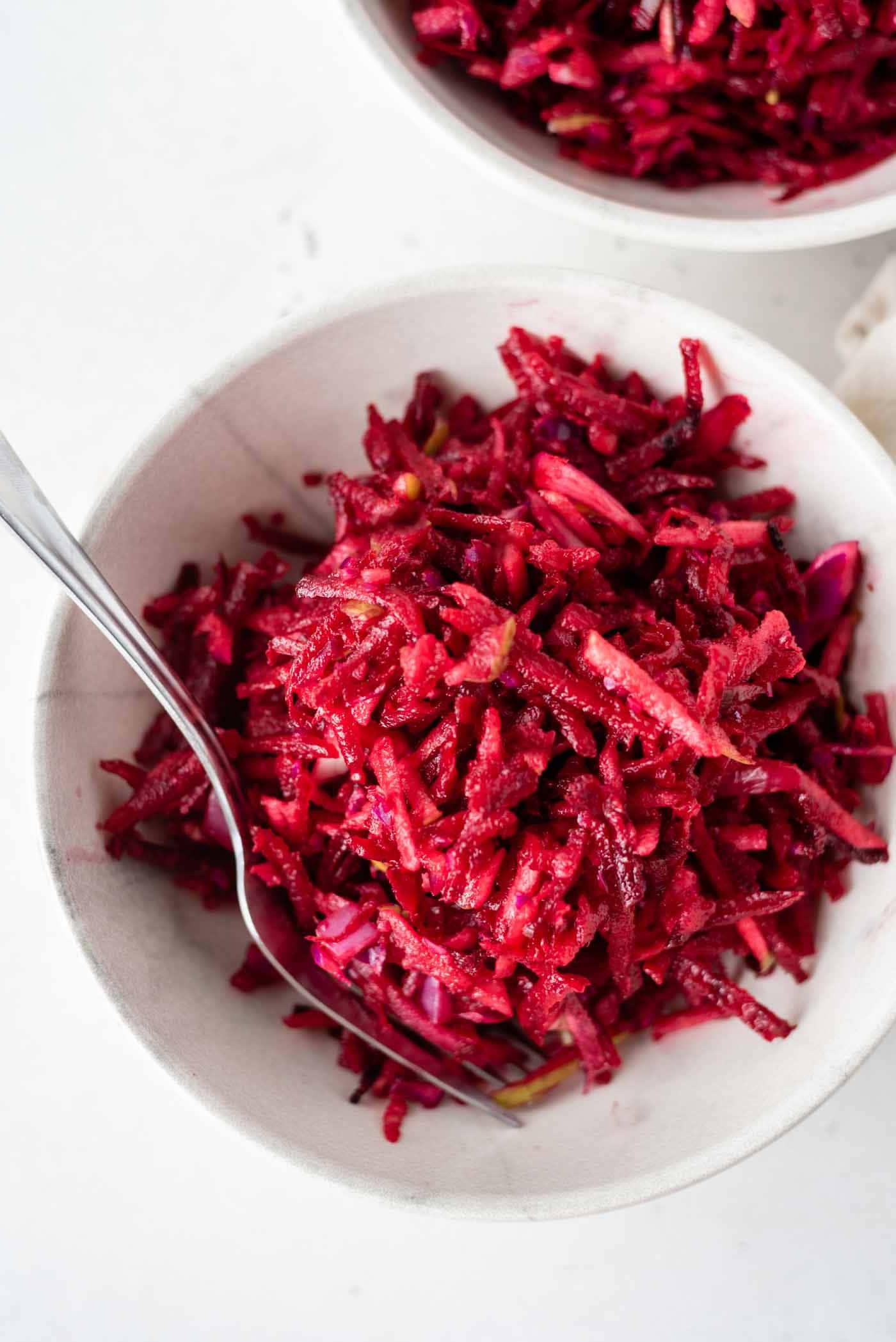 Appel Beet Slaai 2 ’n Bo-aansig van ’n beetslaai met appel en kool in ’n bak met ’n vurk.
