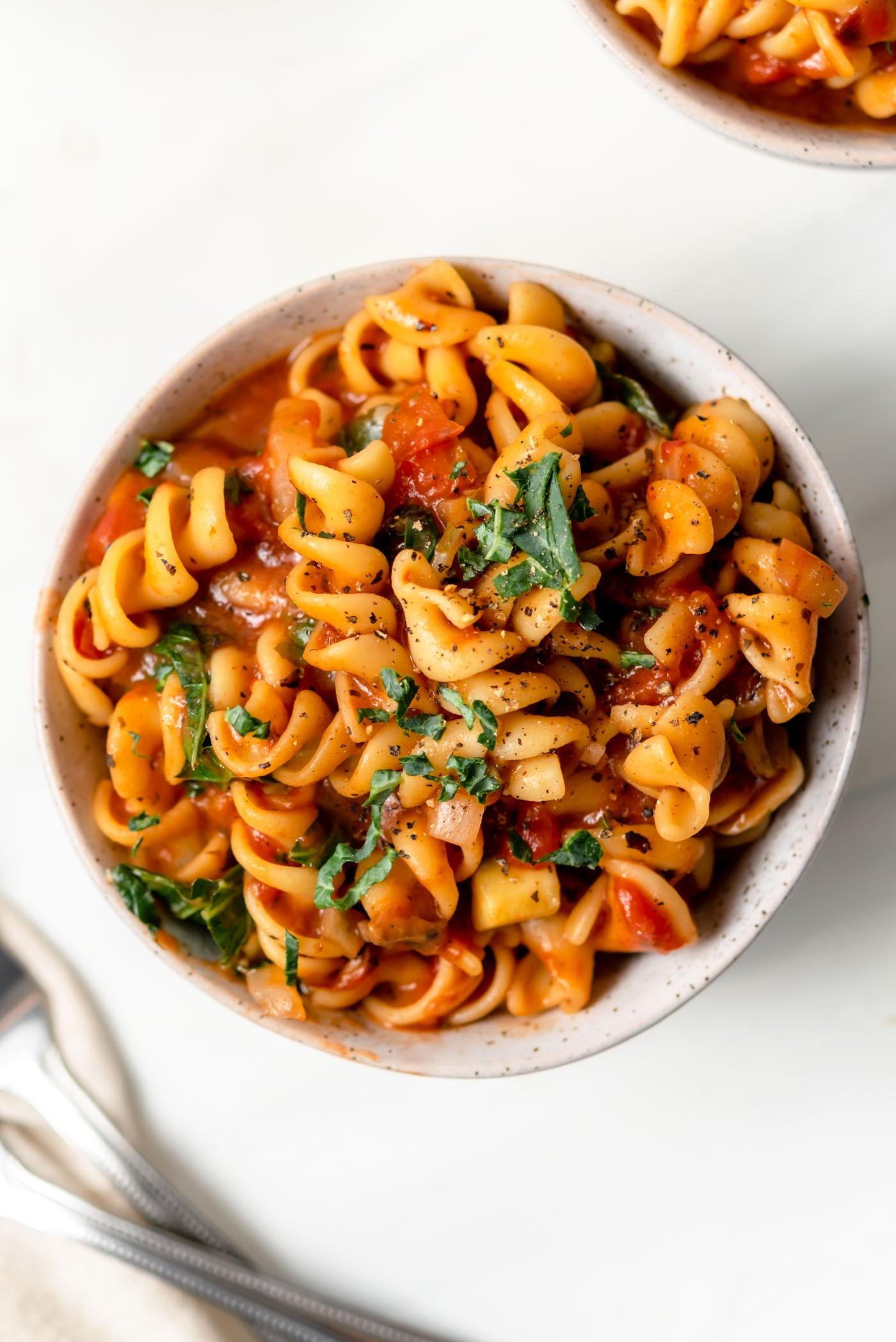 Vegan Een-pot Pasta 2 A bowl of rotini pasta in tomato sauce and vegetables like chopped mushroom, onion, bell pepper and zucchini.