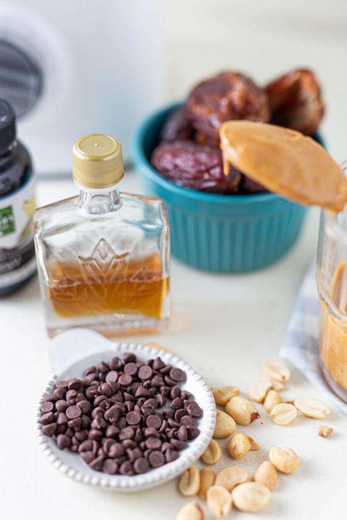 Chocolate chips, maple syrup and dates in containers on a white surface.