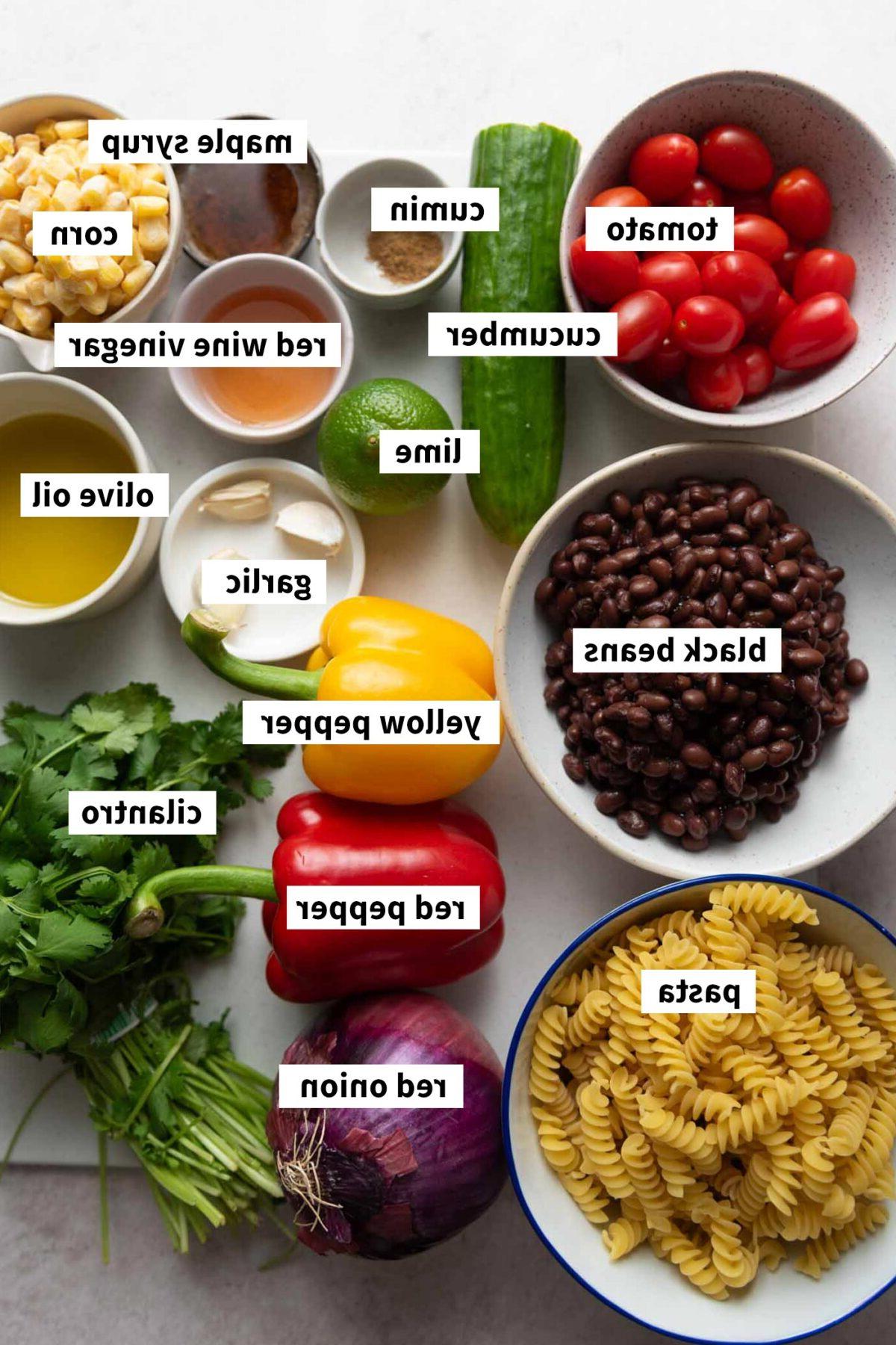 Swartboontjie Pastaslaai 3 Al die bestanddele benodig vir 'n swartboontjie pasta mielieslaai met tamatie en komkommer, elkeen gemerk met teks.