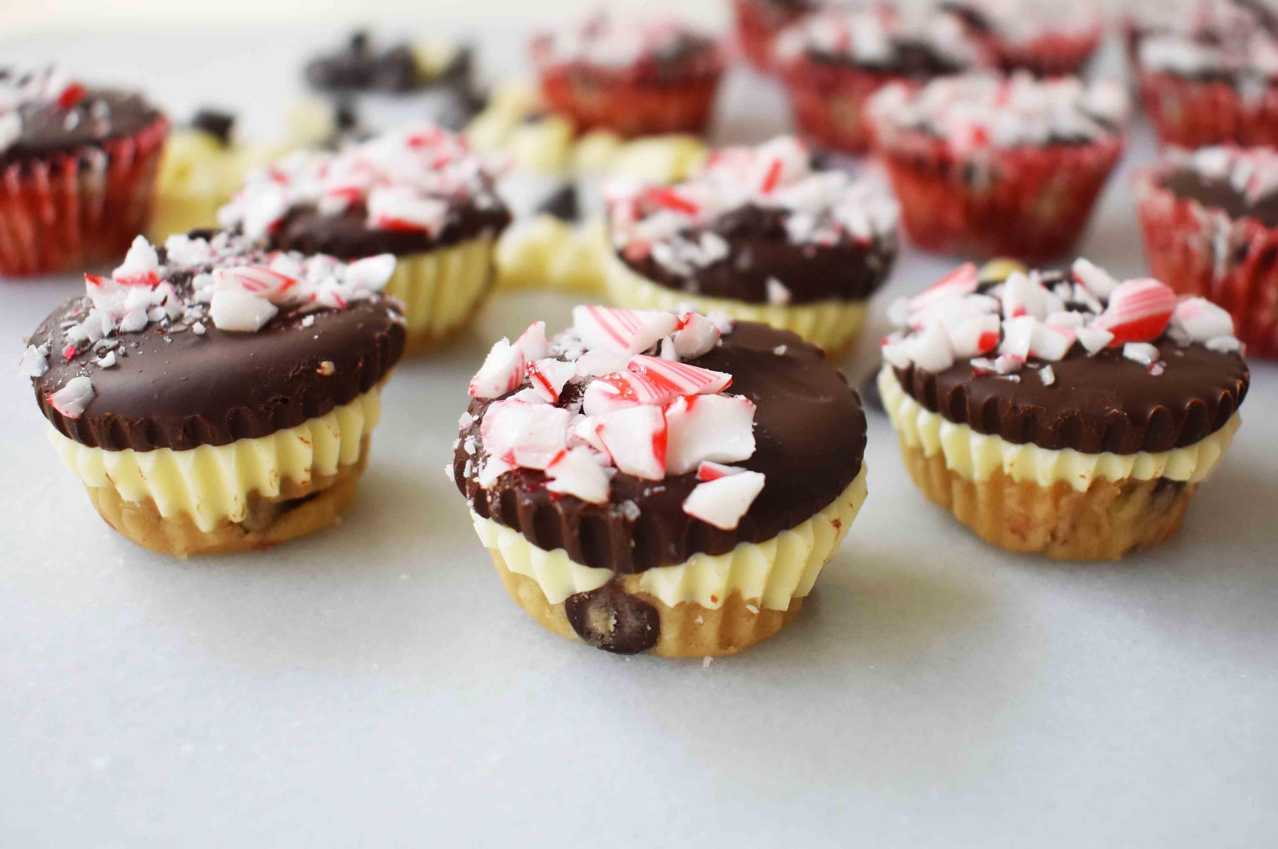 Κυπελλάκια Ζύμης Μπισκότου Peppermint Bark από το Modern Honey. Ζύμη μπισκότου με κομματάκια σοκολάτας χωρίς αυγά, στρωμένη με λευκή σοκολάτα και ημίγλυκη σοκολάτα, και γαρνιρισμένη με τριμμένα ζαχαρωτά μπαστούνια.