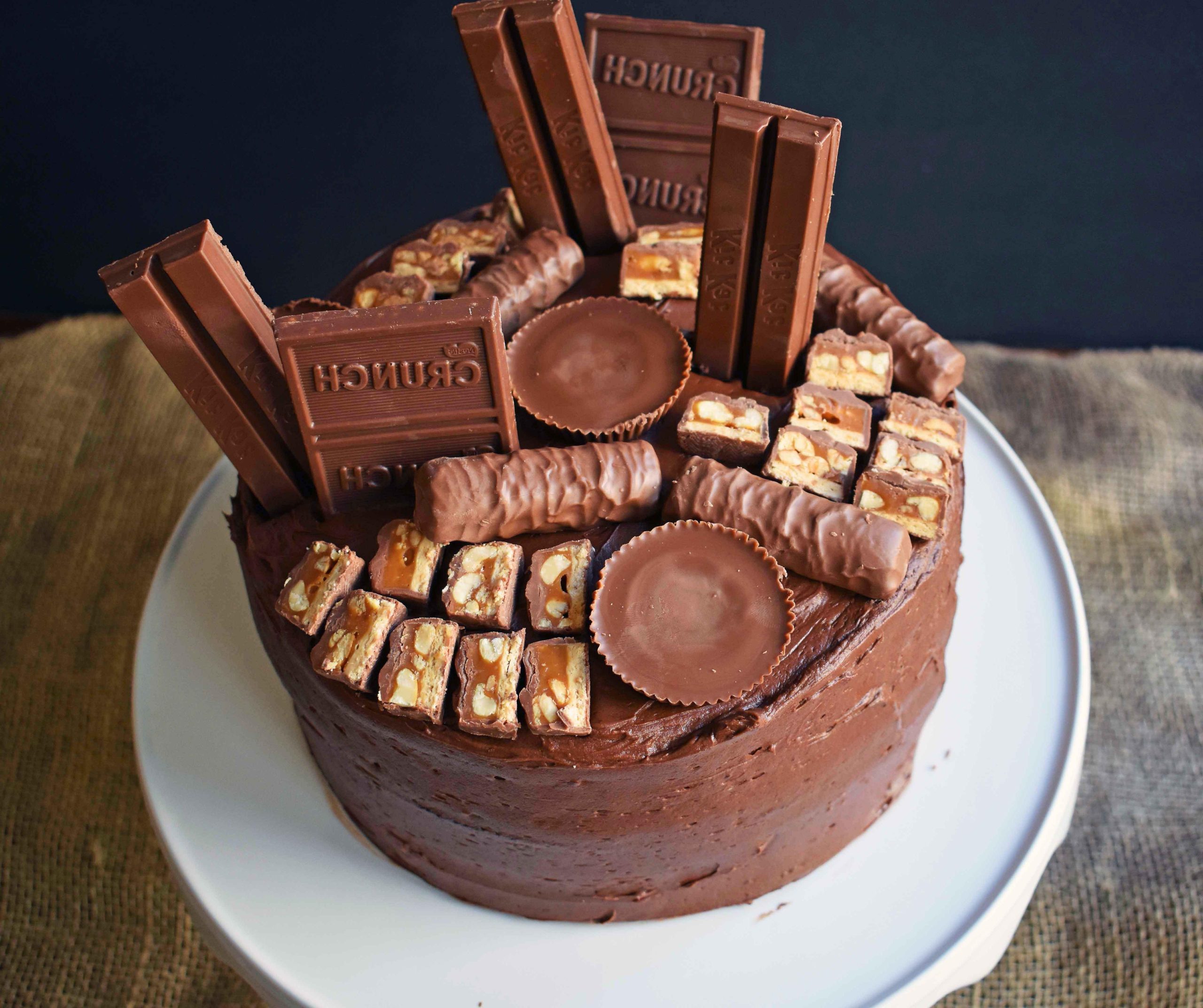 Candy Bar Stash Chocolate Cake by Modern Honey. Perfect chocolate cake topped with chocolate buttercream and the most popular candy bars. It's the ultimate Chocolate Candy Bar Cake.