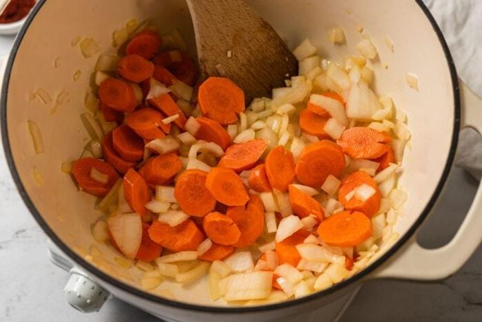 Suurlemoenlensiesop 4 Ui, knoffel en wortel wat in 'n groot soppot met 'n houtlepel kook.
