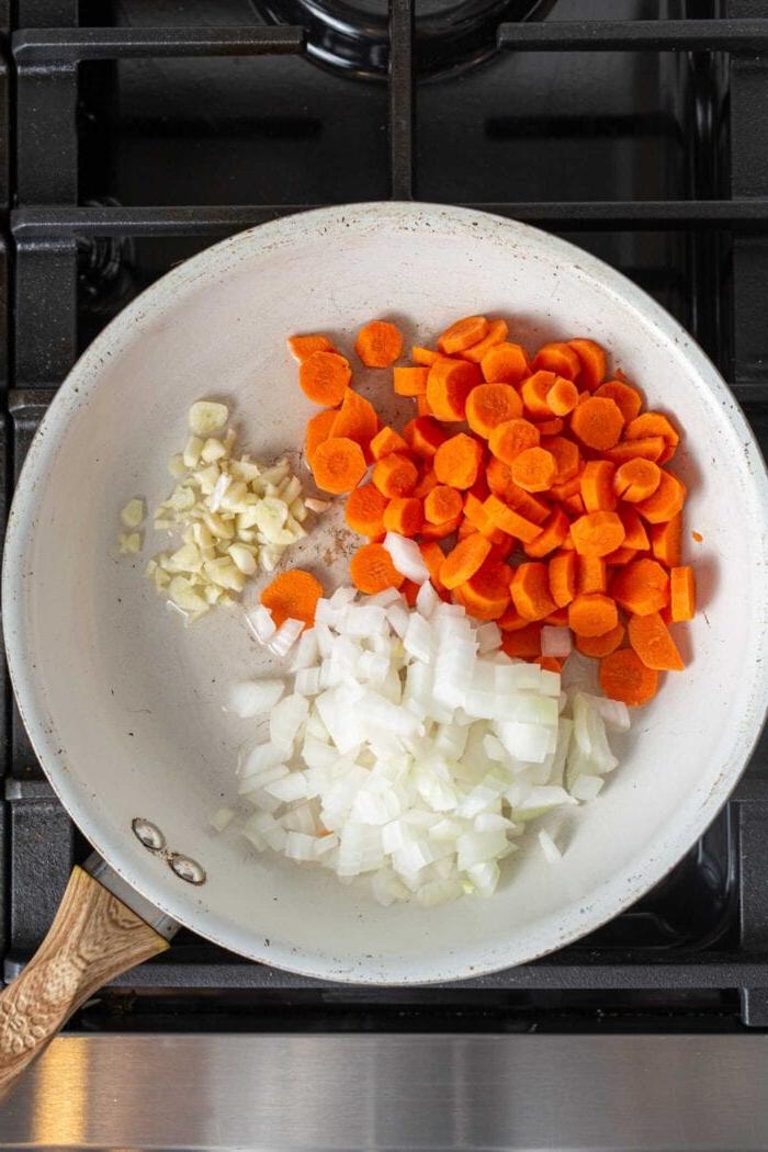 Vegans Panang Kerrie met Tofu 4 Gesnyde uie, knoffel en wortels wat in 'n pan op 'n stoof kook.