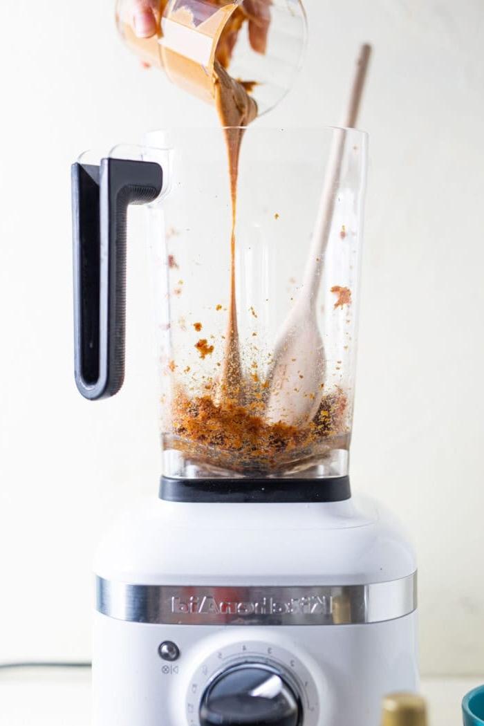 Almond butter being poured into a blender with blended dates in it.