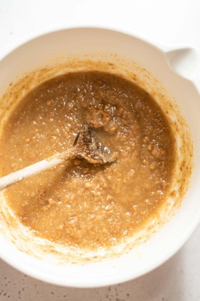 Vegan Proteïen Muffins 4 Amandelbotter wat met appelmoes en esdoornstroop in 'n mengbak met 'n lepel gemeng word.