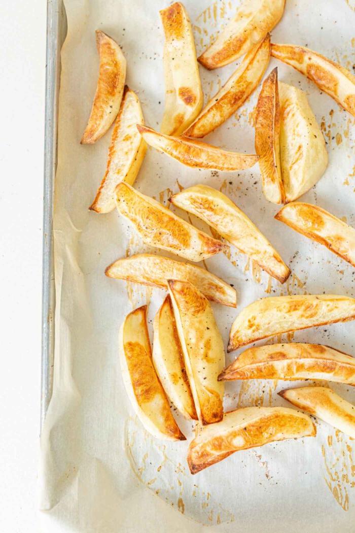 Veganes Chili Kaas Tjips 4 Gebakte patatjies op 'n bakplaat wat met bakpapier uitgevoer is.