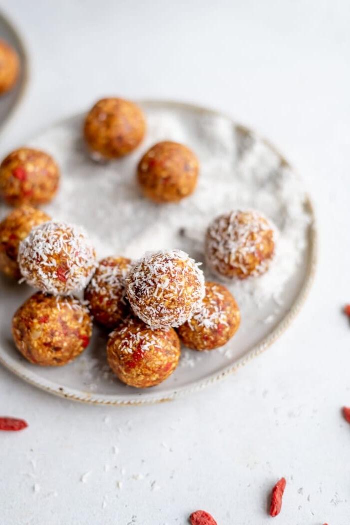 Ongebakte Gojibessie Balletjies 5 Orange energy balls rolled in coconut on a small plate with some goji berries in the foreground.