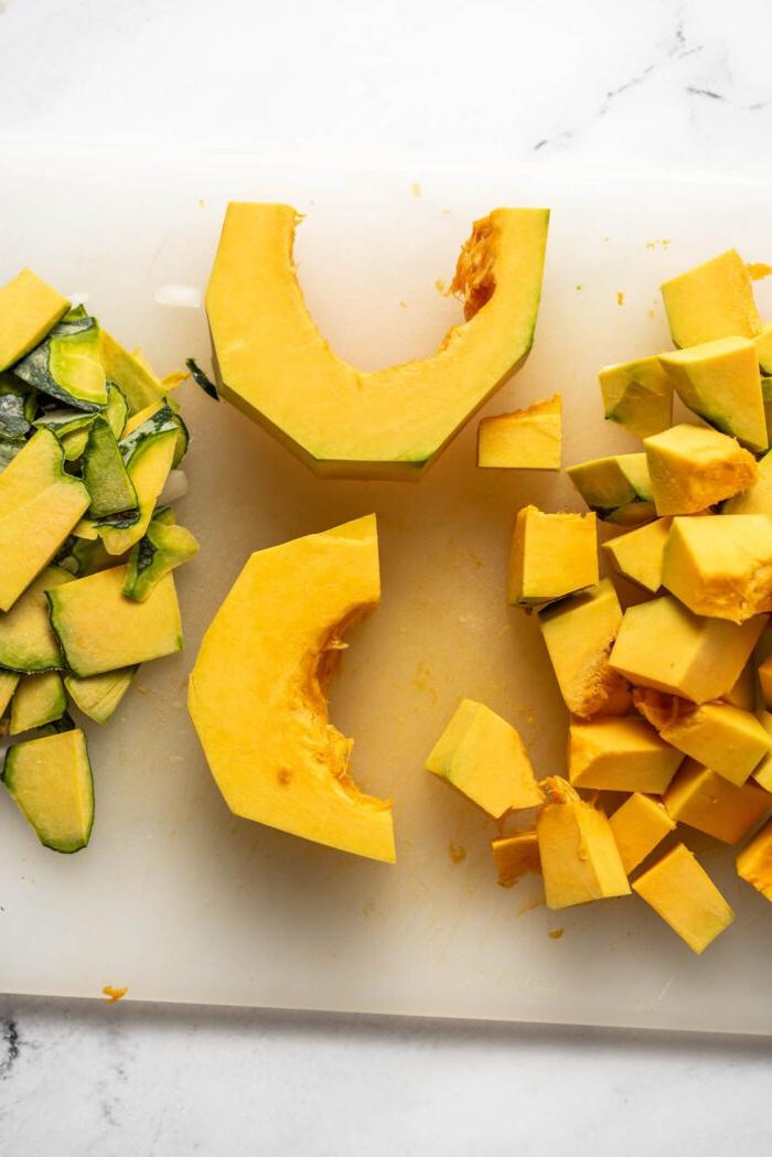 Wiggies van kabocha pampoen in blokkies gesny op 'n snyplank.