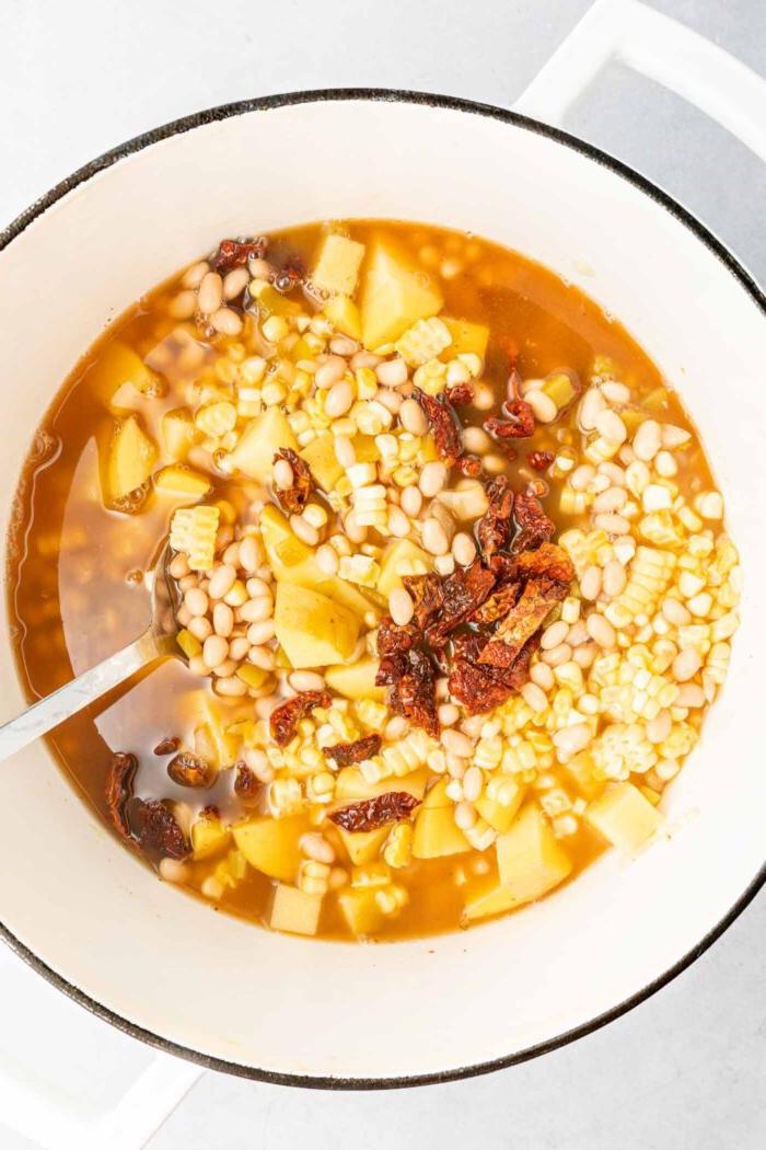 Vegan Somer Mielieroomop 5 'n Groot sopbak met mielies, songedroogde tamaties, aartappels, witbone en bouillon. 'n Lepel rus in die pot.