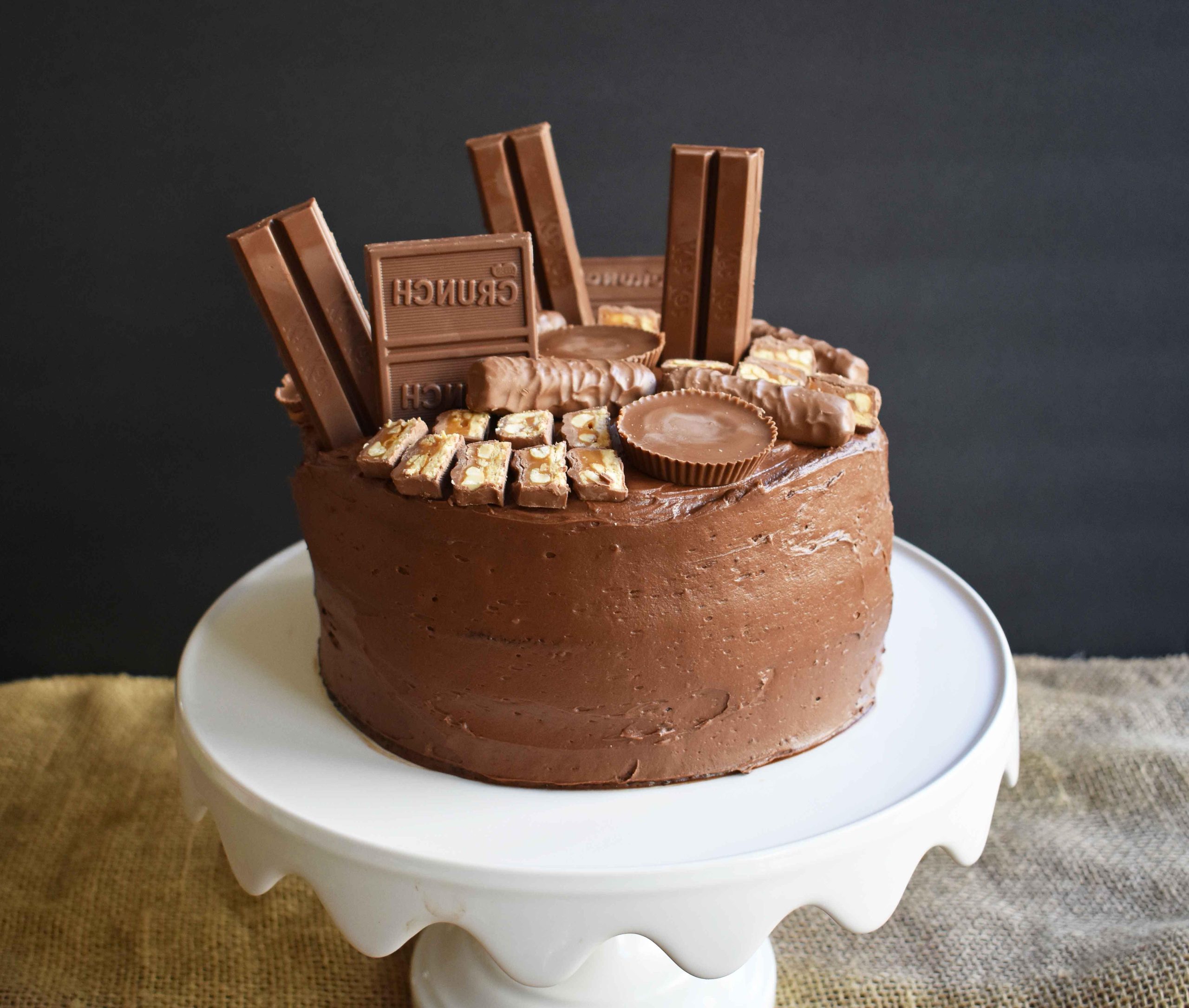 Candy Bar Stash Chocolate Cake by Modern Honey. Perfect chocolate cake topped with chocolate buttercream and the most popular candy bars. It's the ultimate Chocolate Candy Bar Cake.