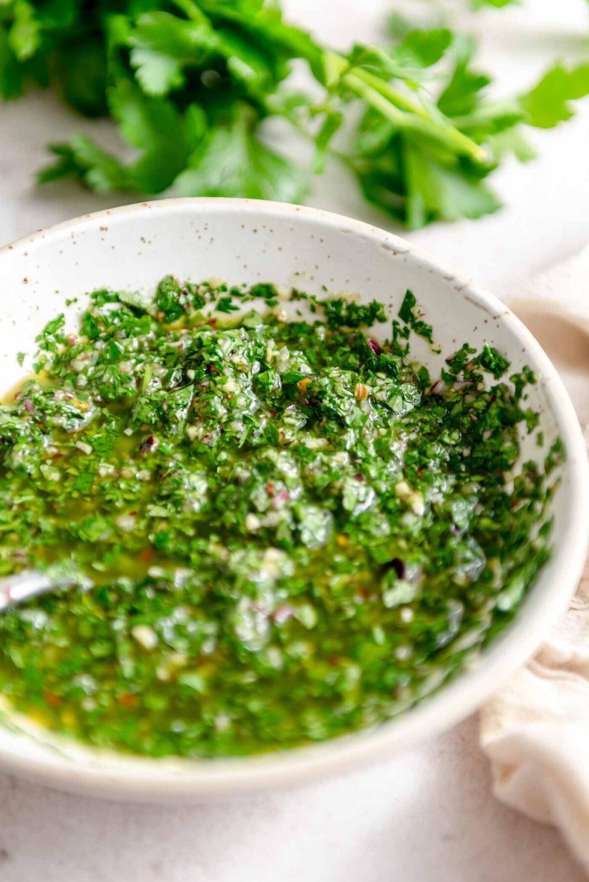 Koriander Tjimmitsjoerri Sous 6 Bak chimichurri sous met 'n lepel daarin en vars kruie in die agtergrond.