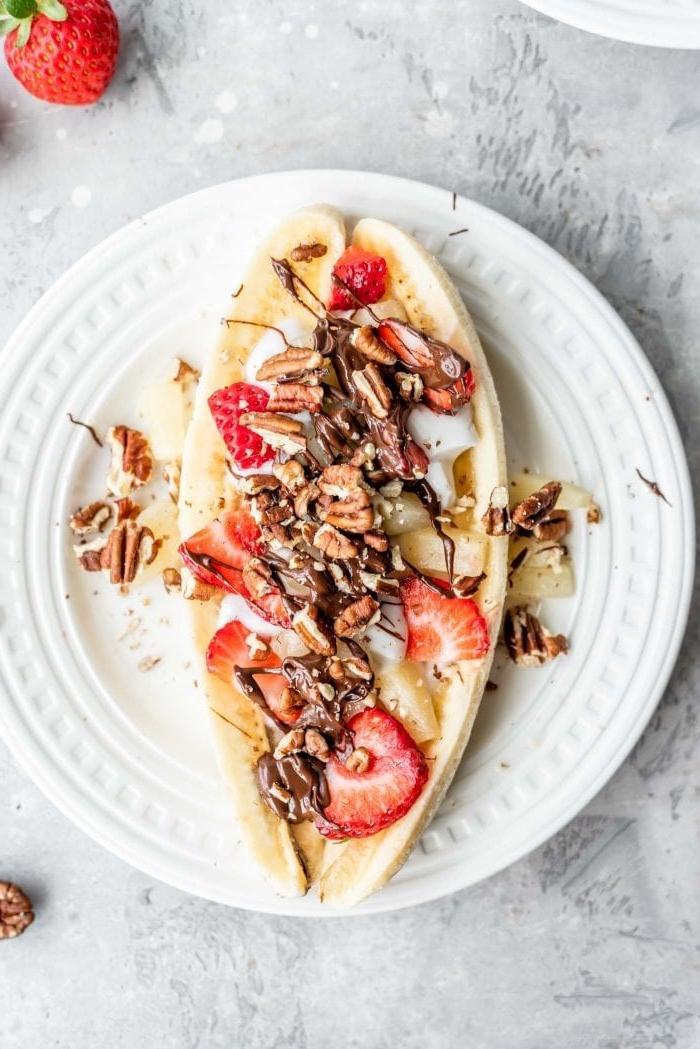 Gesonde Veganistiese Piesangsplit 6 ’n Vegan piesangsplit met suiwelvrye jogurt, pekannote en aarbeie op ‘n wit bord.