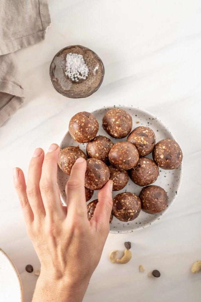 Maca Sjokoladestukkies Energie Balletjies 7 ’n Hand gryp 'n energiebal van 'n bord af, wat die gereed-vir-eet-fase aandui.