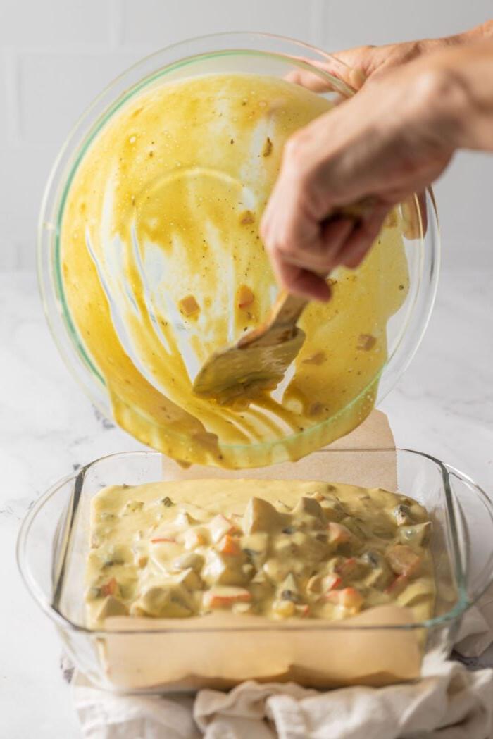 Gooi eieraartappel kasserolbeslag uit 'n bak in 'n vierkantige glasbakpan.