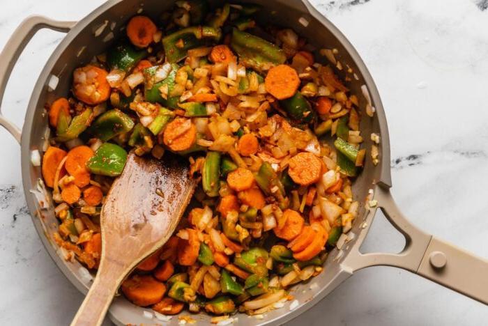 Wortel, soetrissie en ui wat in rooikerriepasta in 'n pan kook.