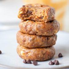 A stack of 4 raw peanut butter cookie with a few chocolate chips sprinkled around them.