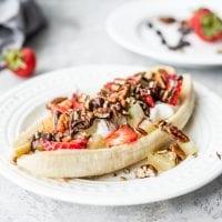 Gesonde Veganistiese Piesangsplit 7 ’n Vegan piesangsplit met suiwelvrye jogurt, pekannote en aarbeie op ‘n wit bord.