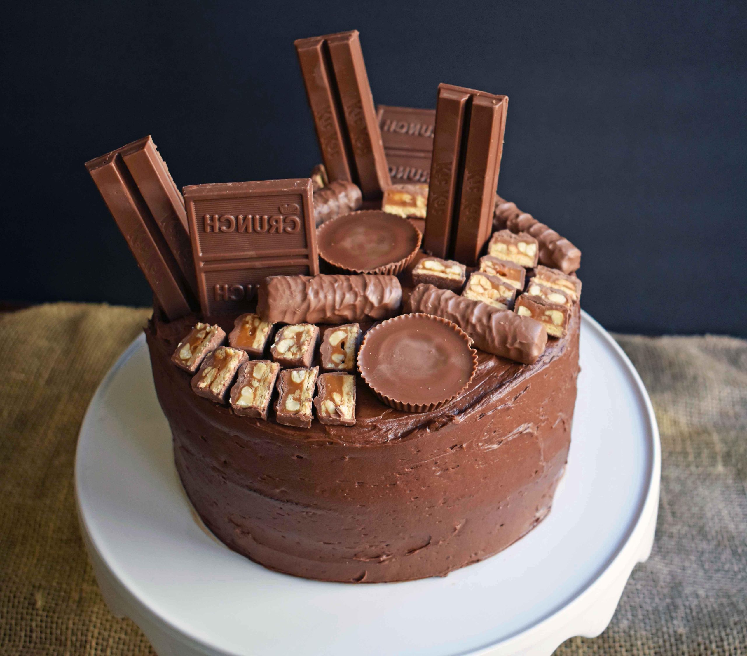 Candy Bar Stash Chocolate Cake by Modern Honey. Perfect chocolate cake topped with chocolate buttercream and the most popular candy bars. It's the ultimate Chocolate Candy Bar Cake.