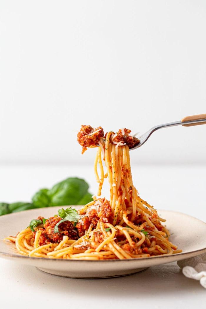 Gaffel wat spaghetti en sampioen bolognese sous met basiliekruid oplig van 'n klein bord.