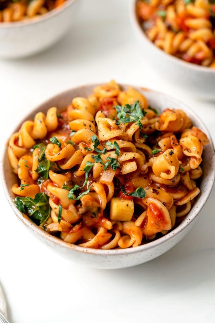 Vegan Een-pot Pasta 9 Bowl of pasta noodles with tomato vegetable sauce and fresh chopped herbs on top.