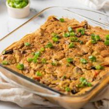 Gebakte vegan aartappel eierkasserol in 'n glasbakskottel. Klein bakkie gesnyde avokado is in die agtergrond.
