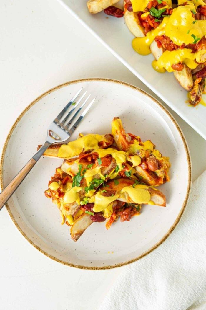 Veganes Chili Kaas Tjips 10 ’n Klein bord gebakte patatjies bedek met chili en kaassous.