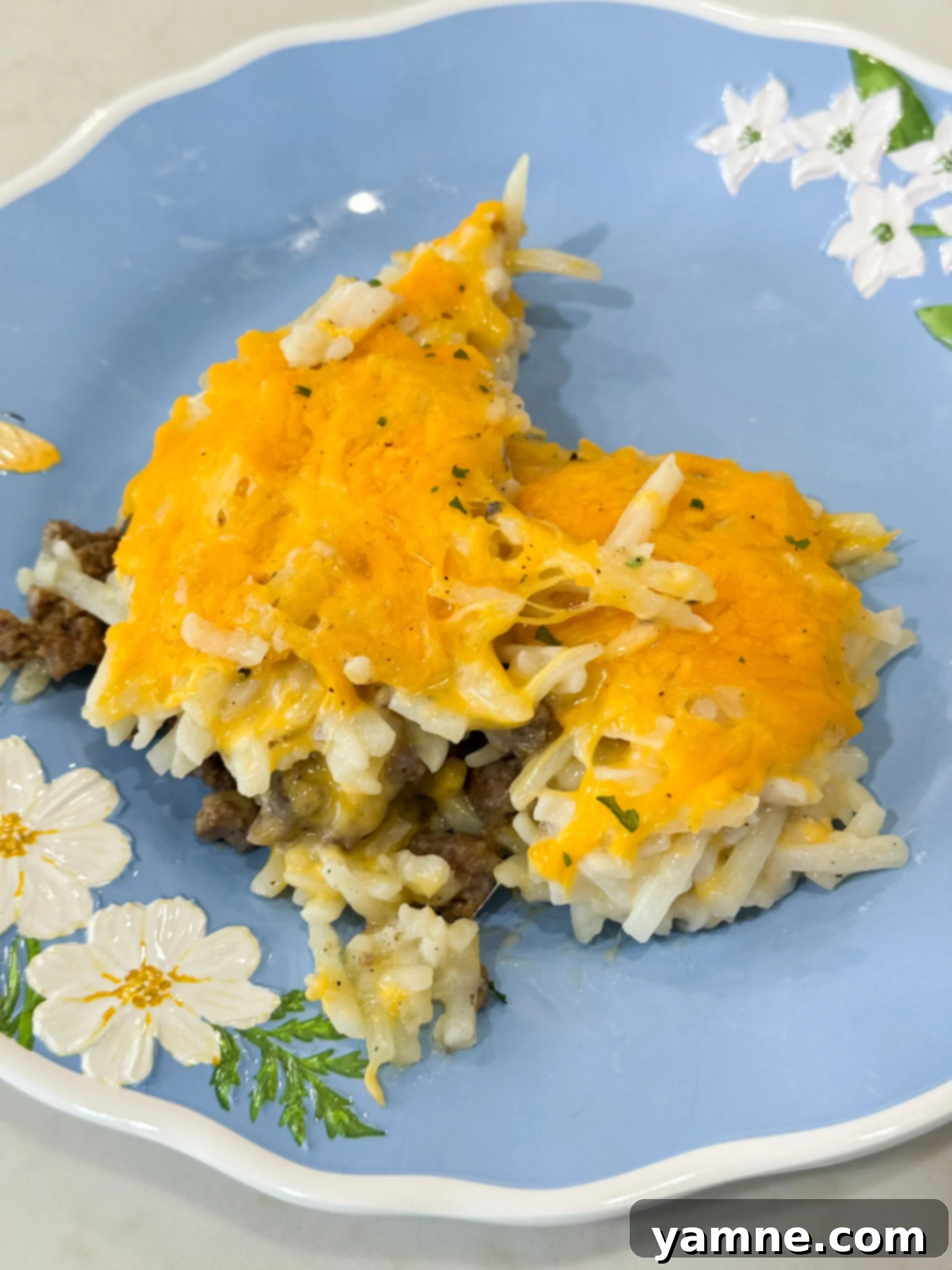Baked hashbrown hamburger casserole on a plate topped with melted cheese