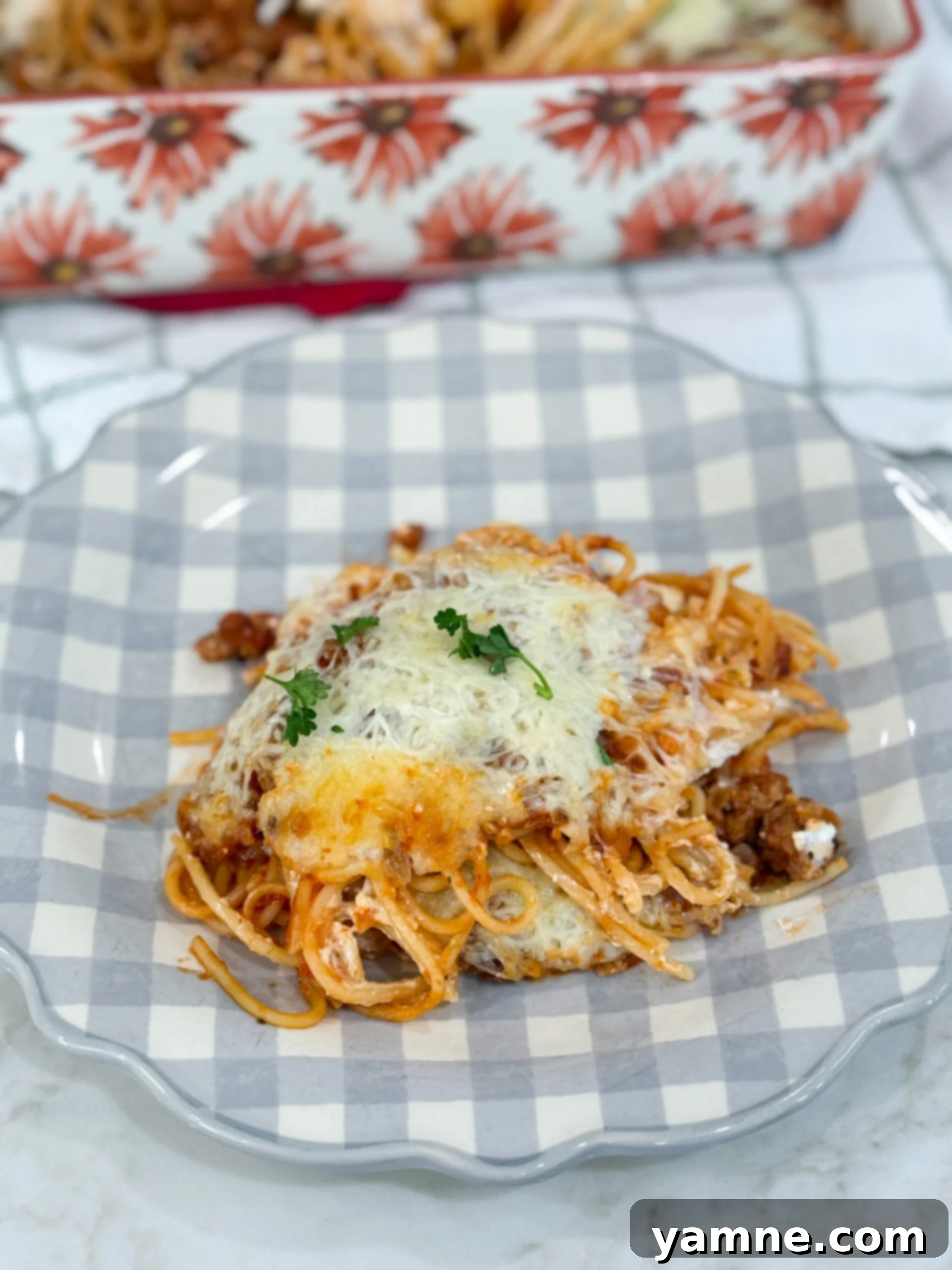 Million Dollar Spaghetti served on a plate with layers of pasta, sausage sauce, and melted cheese, garnished with parsley.