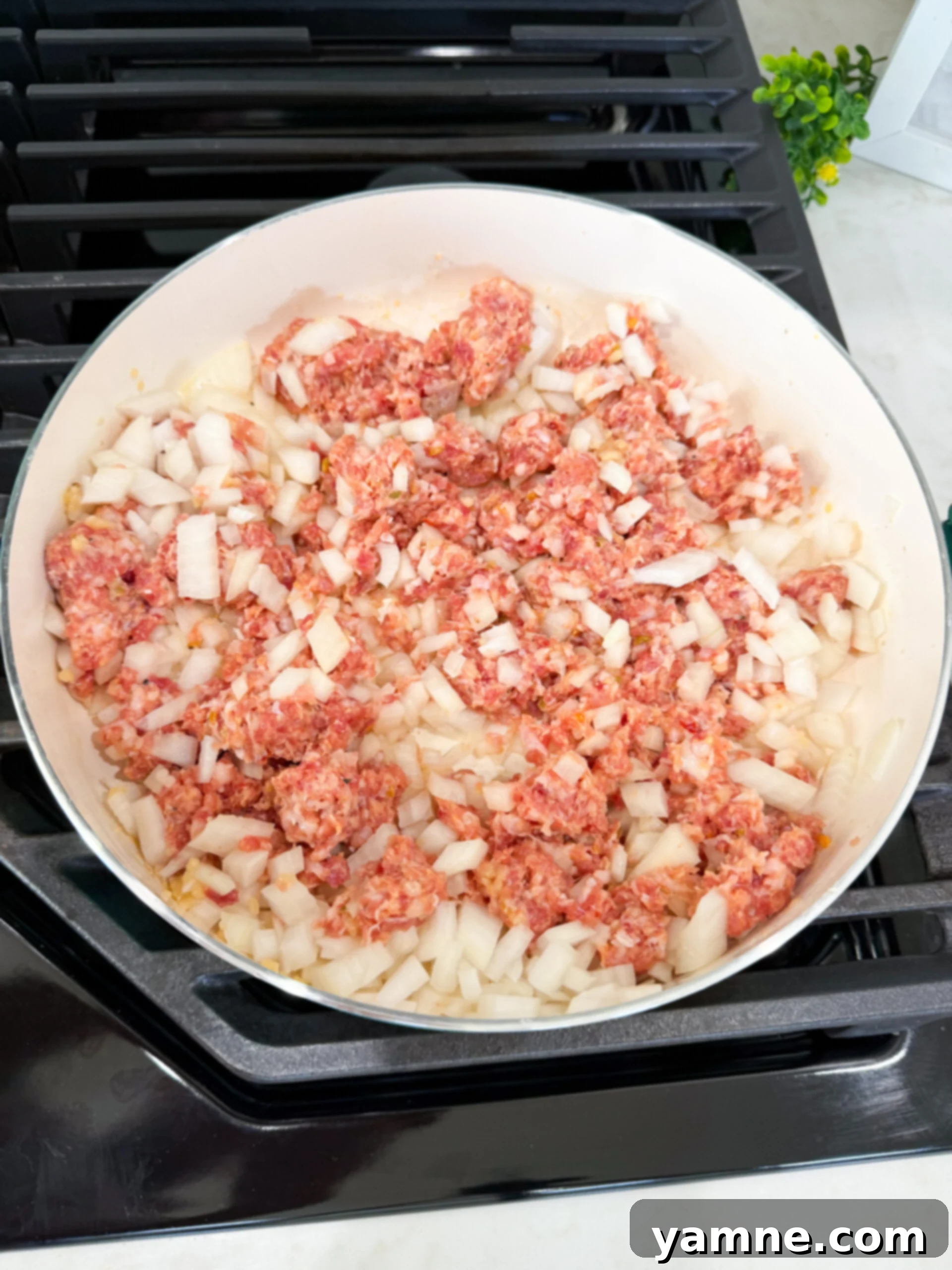 Ground Italian sausage and diced onions cooking together in a skillet for Million Dollar Spaghetti.