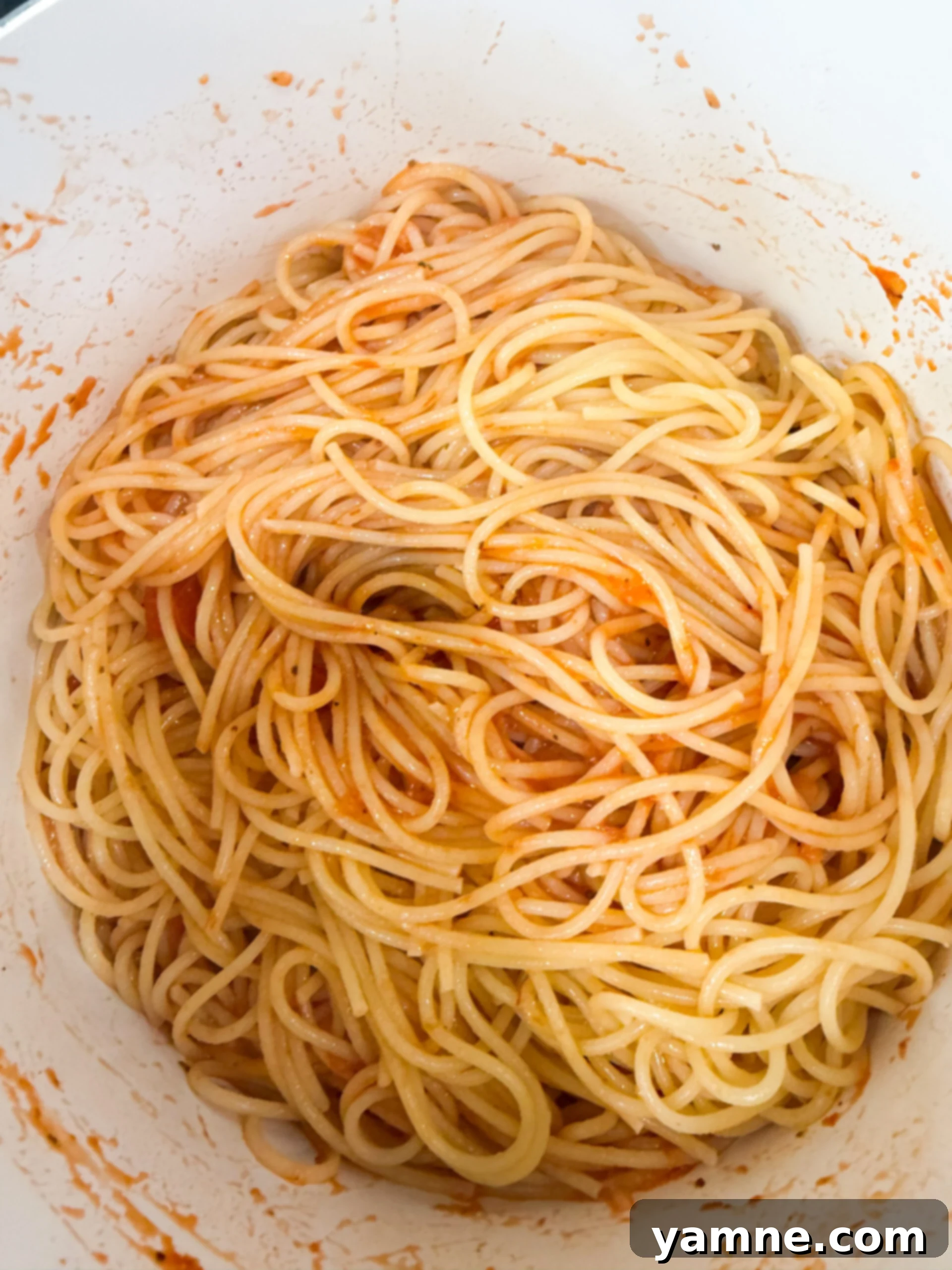 Cooked spaghetti tossed with marinara sauce in a large pot.