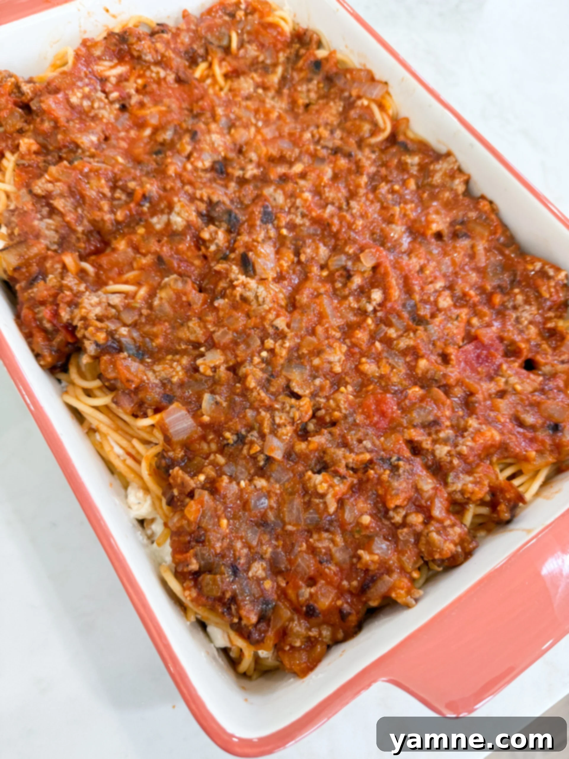 Cooked sausage and marinara mixture spread evenly over spaghetti layers in casserole dish.
