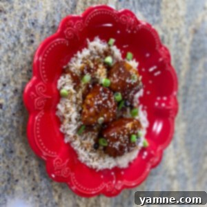 Delicious Slow Cooker Sesame Chicken served over white rice with sesame seeds and green onions.