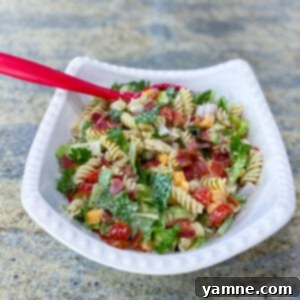 Freshly prepared BLT Pasta Salad, showing rotini pasta, crispy bacon, cherry tomatoes, and green romaine lettuce with a creamy dressing.
