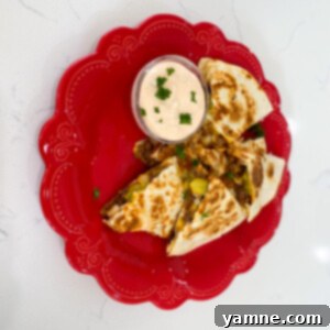 Two halves of crispy cheeseburger quesadillas served with a side of special sauce, on a plate.