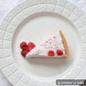 Refreshing Raspberry Lemon No-Bake Cheesecake 2 A slice of Raspberry Lemon No-Bake Cheesecake on a white plate, garnished with fresh raspberries and lemon zest.