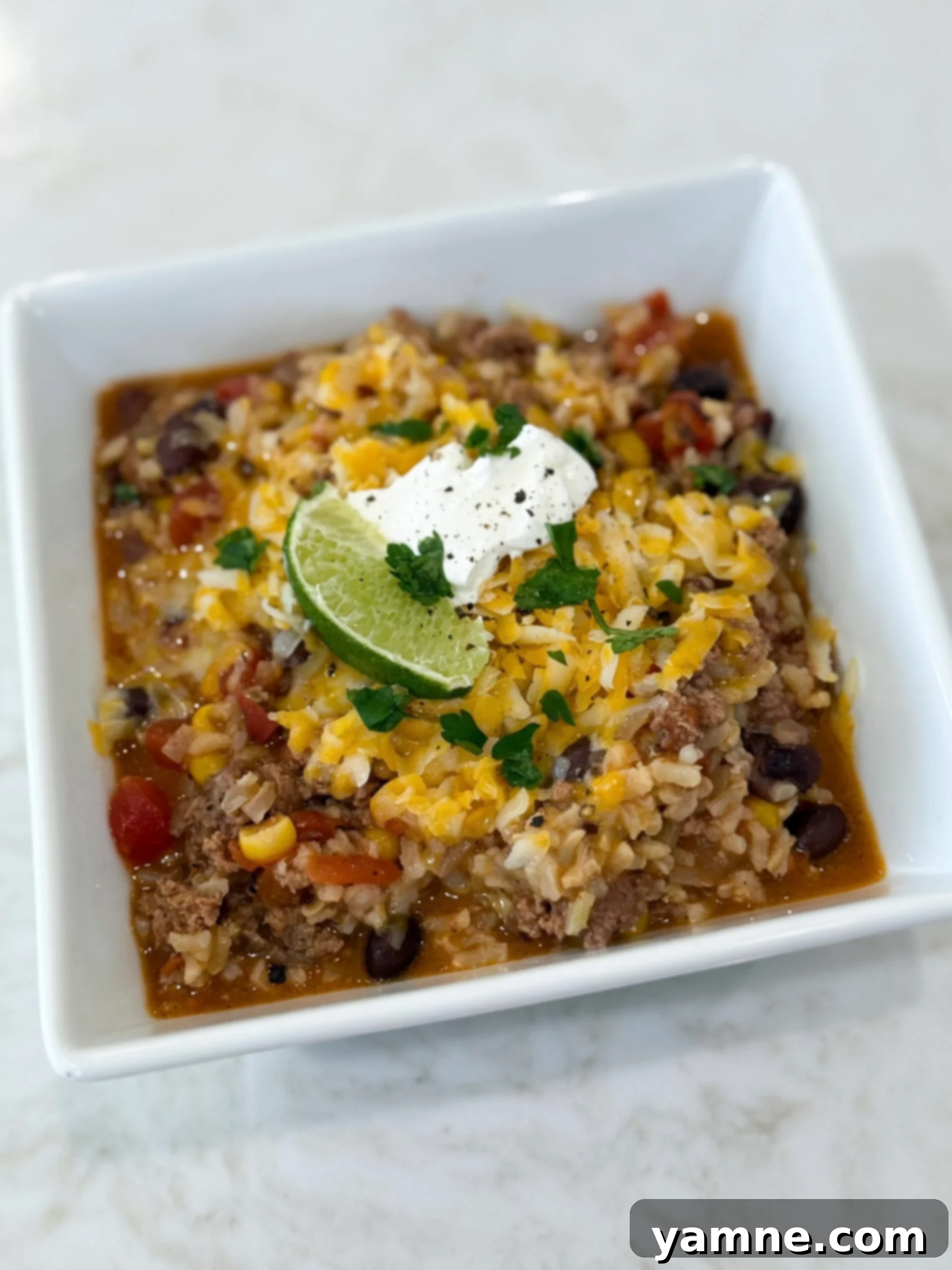 A vibrant bowl of Mexican beef and rice one-pot meal, generously topped with creamy avocado slices and a dollop of sour cream, ready to be enjoyed.