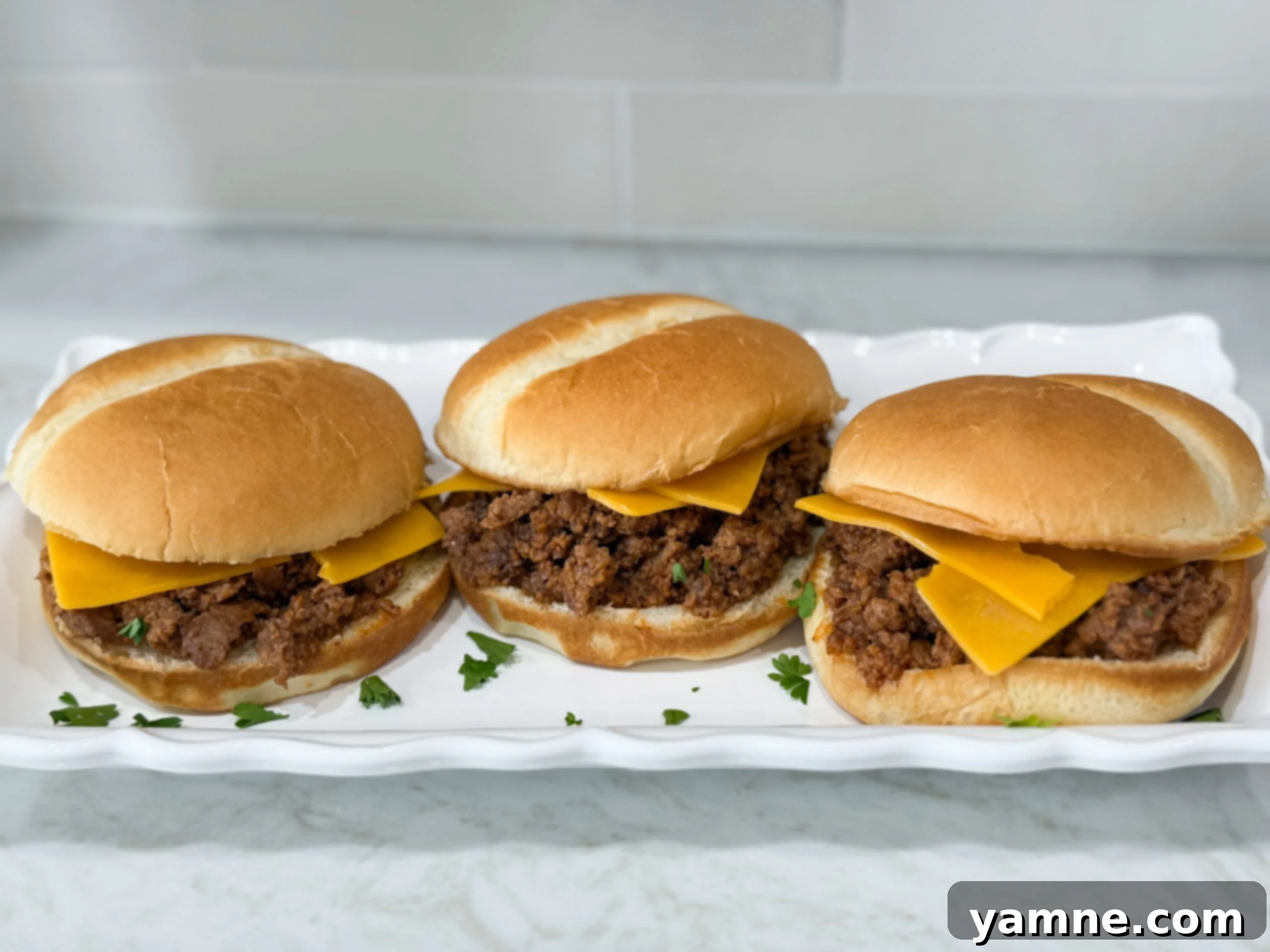 Simple Sloppy Joe sandwiches with cheese on hambuger buns on a long white plate on top of a white counter