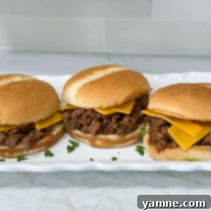 Simple Sloppy Joe sandwiches with cheese on hambuger buns on a long white plate on top of a white counter