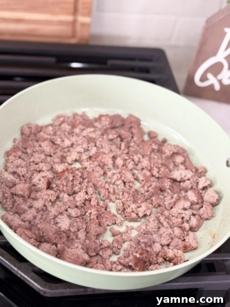 Ground meat cook in a large white skillet on the stove top