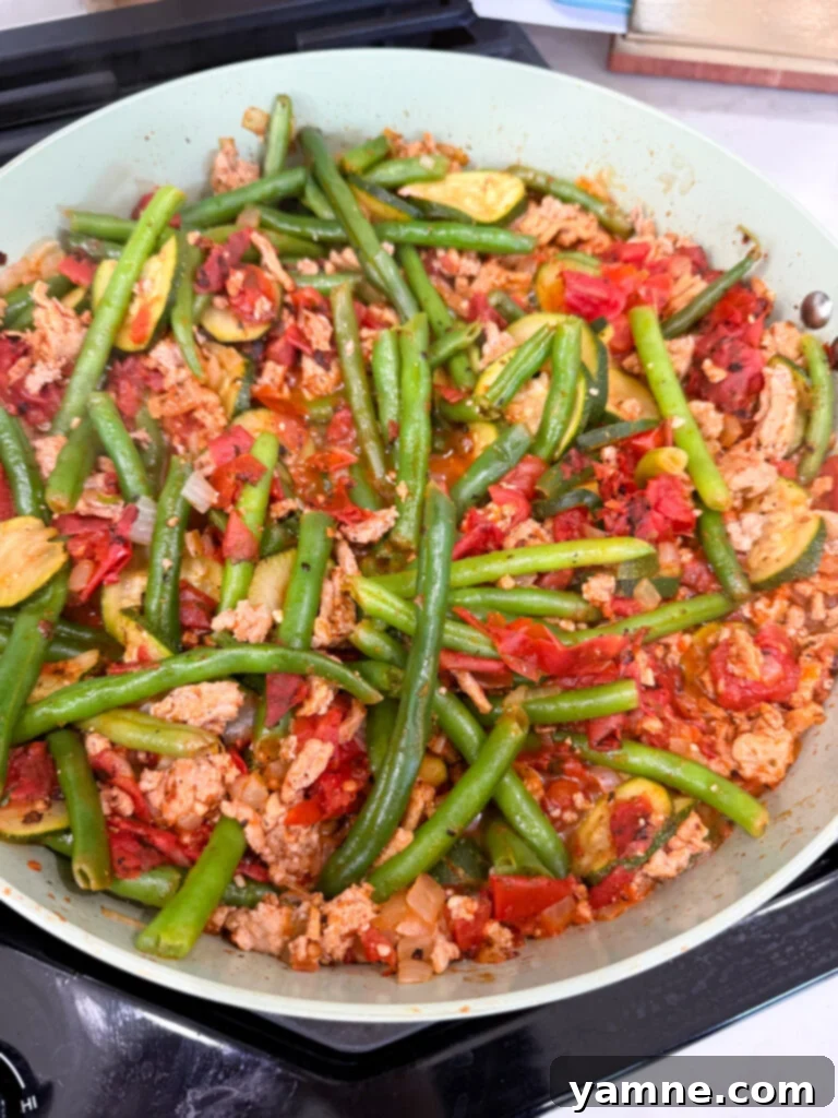 Healthy Turkey and Veggie Skillet 8 Diced tomatoes being stirred into the turkey and vegetable mixture in the skillet