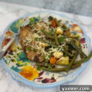 A vibrant sheet pan meal with sliced chicken breast, cherry tomatoes, zucchini, and green beans, topped with Parmesan cheese.