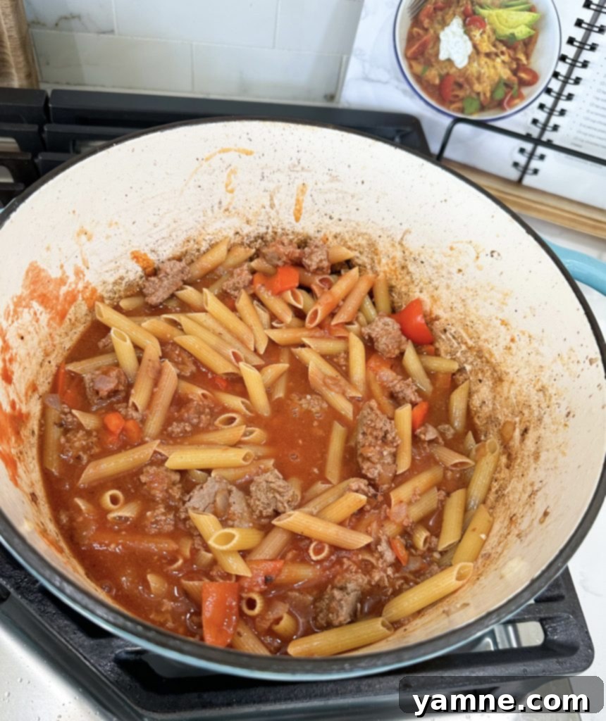 Cooking ground turkey and vegetables with spices in a large pot for pasta.