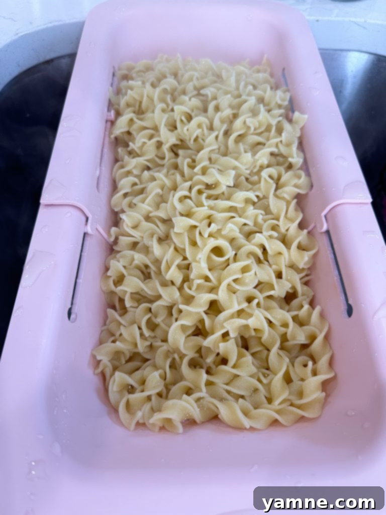Egg noodles being drained in a colander after cooking, steam rising gently.