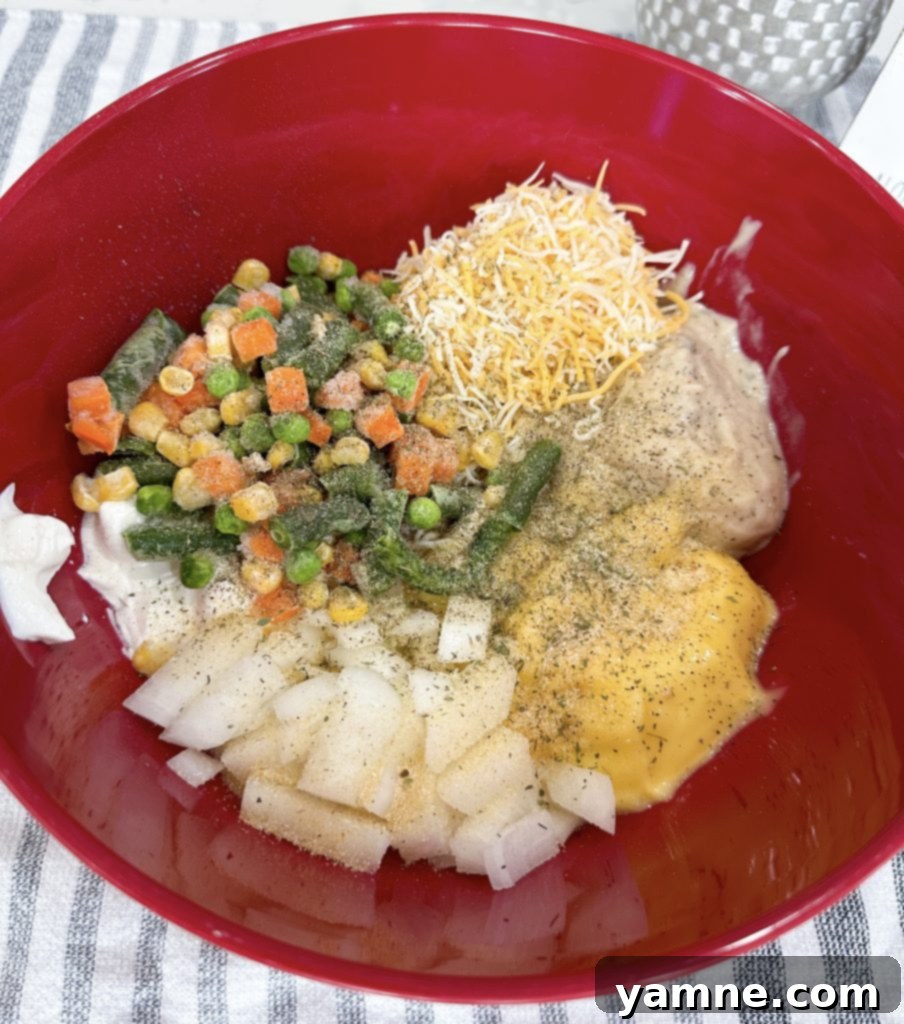 A large mixing bowl filled with creamy casserole ingredients, including condensed soups, chicken, vegetables, and spices, being stirred together before baking.